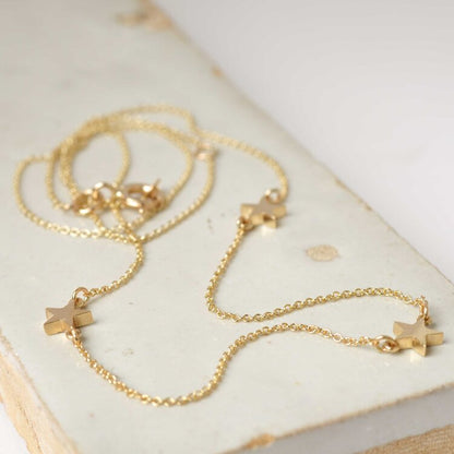A solid gold three-star necklace with a delicate trace chain, displayed on a marble surface.