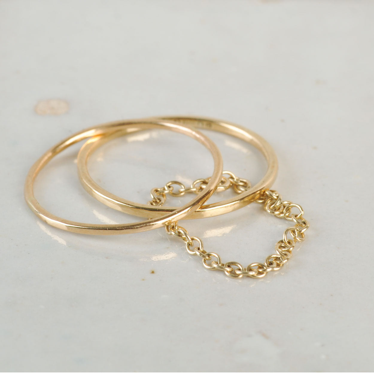 Two gold rings with a chain detail on a light gray background