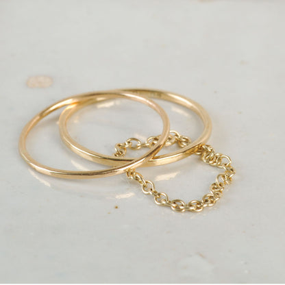 Two gold rings with a chain detail on a light gray background