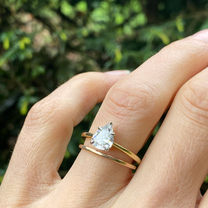 Hand wearing a gold ring with a clear gemstone against a blurred green background