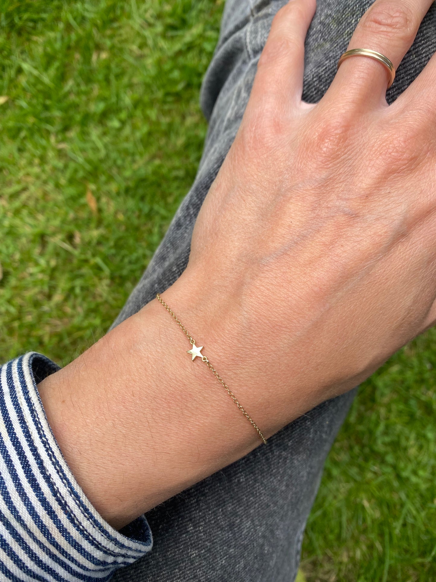 Hand wearing a gold bracelet with a star charm against a grass background