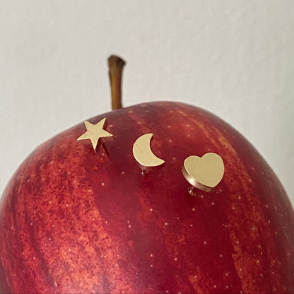 Red apple with gold star, moon, and heart earrings on a white background