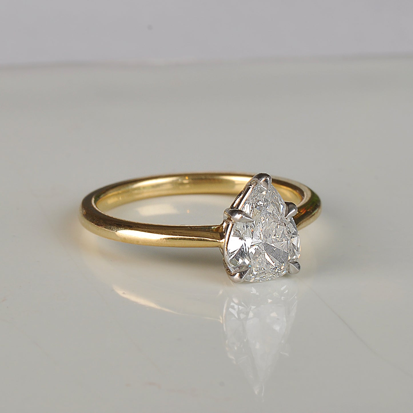 Gold ring with a pear-shaped diamond on a light gray background