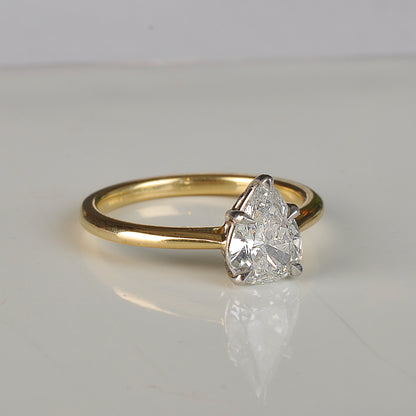 Gold ring with a pear-shaped diamond on a light gray background