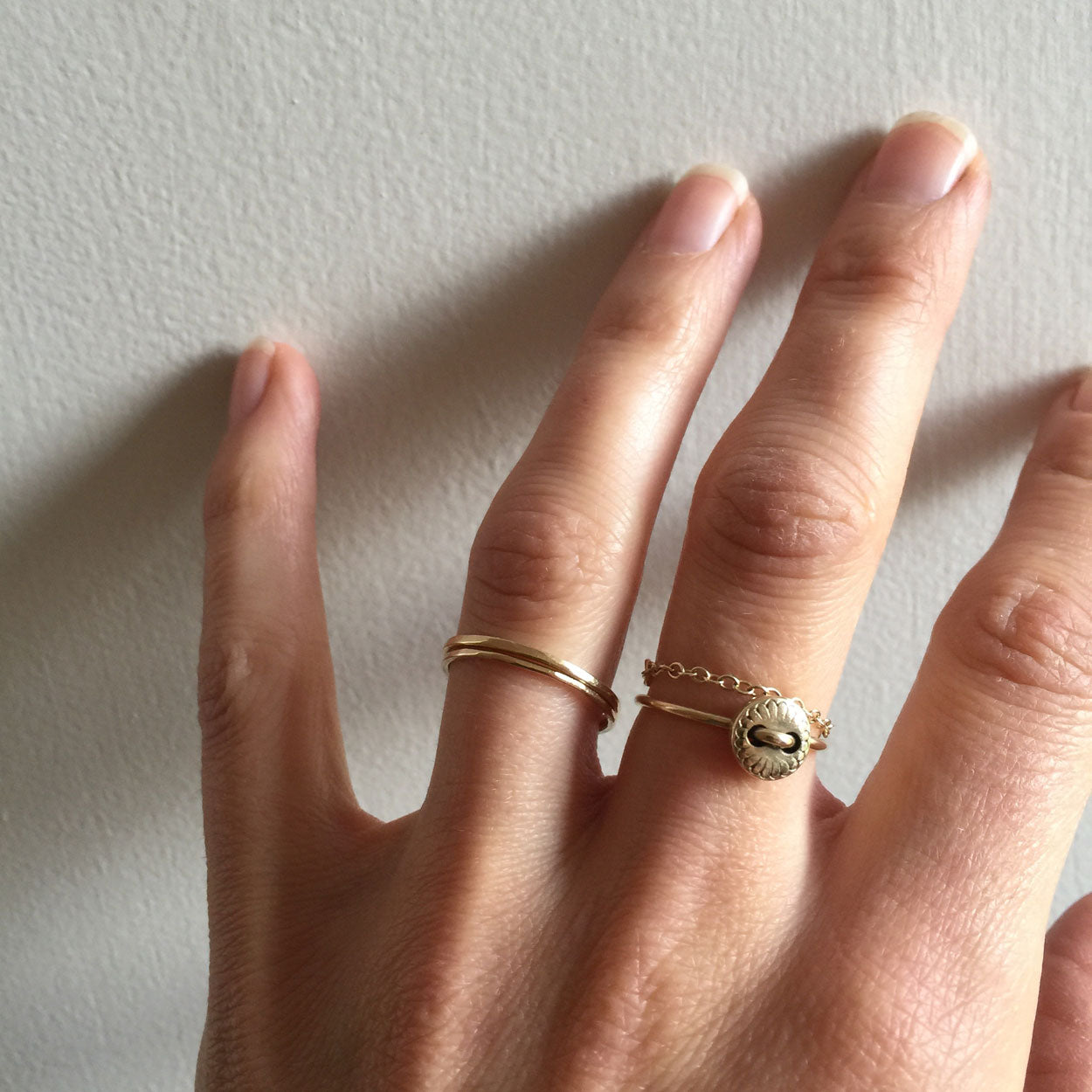Hand wearing two gold rings on a light background