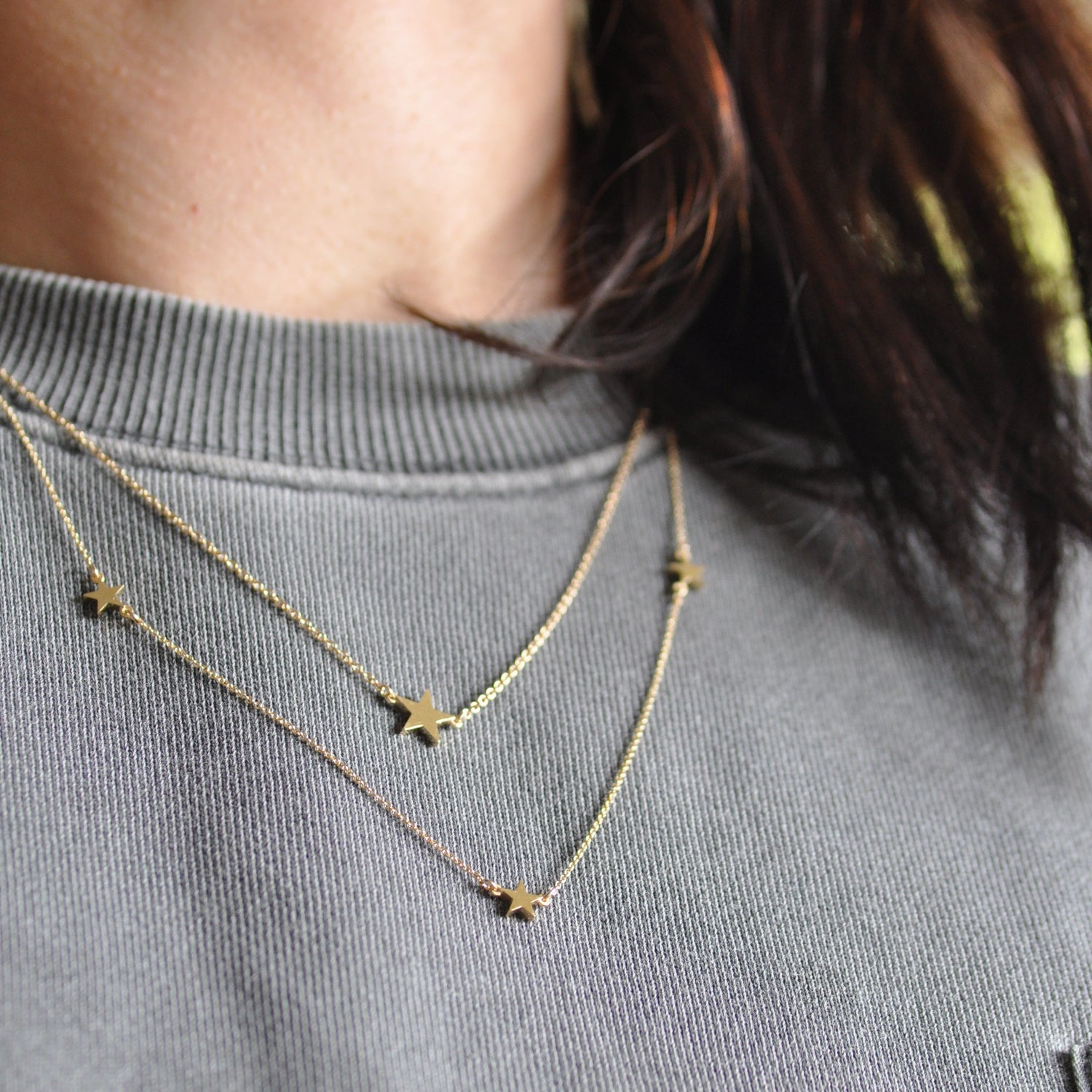 little starts on a fine chain necklace in yellow gold, two star necklaces layered and worn over a grey sweater