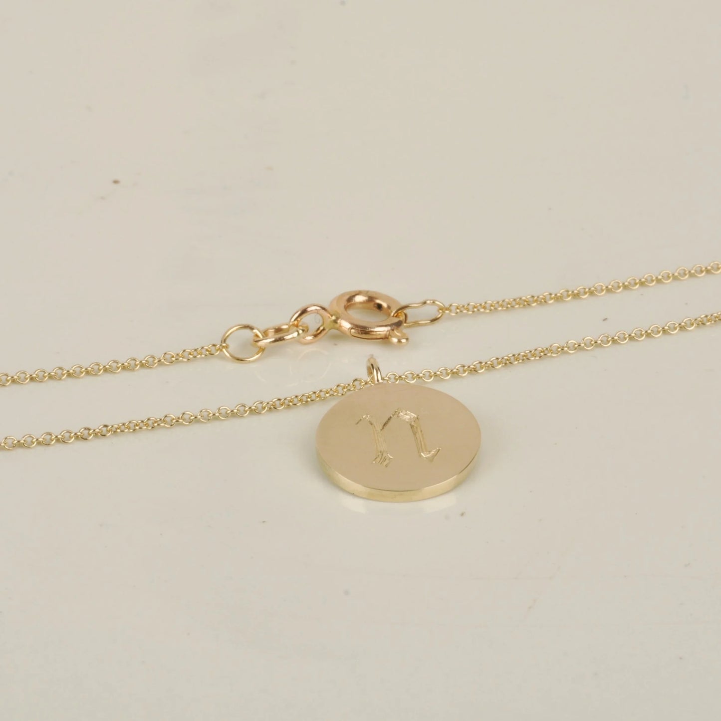 Gold necklace with a round pendant on a light beige background