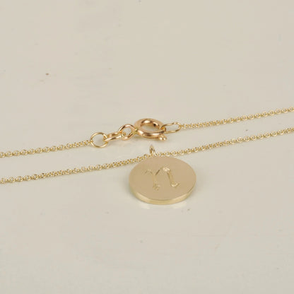 Gold necklace with a round pendant on a light beige background
