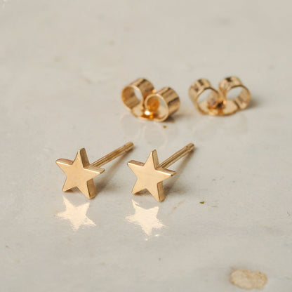 Gold star earrings on a light gray surface