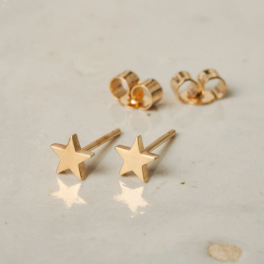 Gold star earrings on a light gray surface